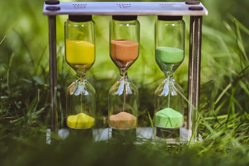 Three hourglasses with yellow, orange and green sand standing in grass