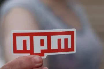 An npm sticker held between two fingers
